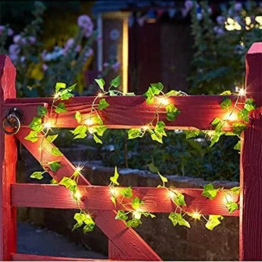 Green Fairy Lights featuring solar-powered warm white LED bulbs intertwined with artificial bright green ivy leaves on a red wooden gate.