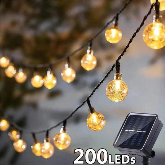 Outdoor Crystal Fairy Lights with warm yellow, crystal-textured round bulbs on black wire and solar panel for outdoor use.