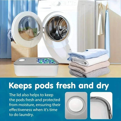 Laundry Pod Container in white and gray plastic with a sliding lid, shown filled with colorful detergent pods next to a washing machine and folded laundry.