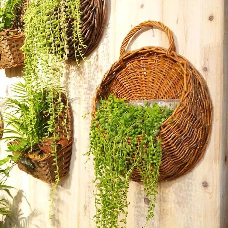 Artificial Plant Vines in green hanging from woven brown wicker baskets with trailing leaves and textured stems on a wooden wall.