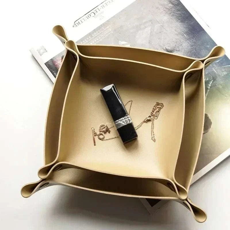 Nordic Leather Desk Tray in beige leather with snap corners, holding a black lipstick and gold necklace on a white surface.