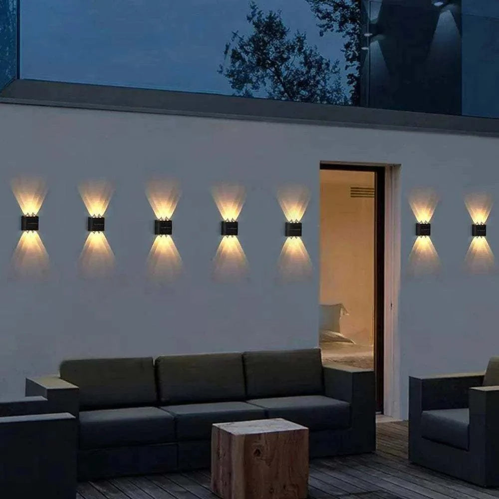 Outdoor Waterproof Fence Lamp in black metal with dual beam warm light pattern mounted on white garden wall above dark outdoor seating