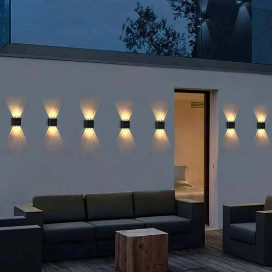 Outdoor Waterproof Fence Lamp in black metal with dual beam warm light pattern mounted on white garden wall above dark outdoor seating