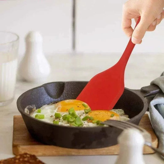 Silicone Cooking Spatula with a red flexible head scraping fried eggs in a black cast iron skillet for easy cooking and serving