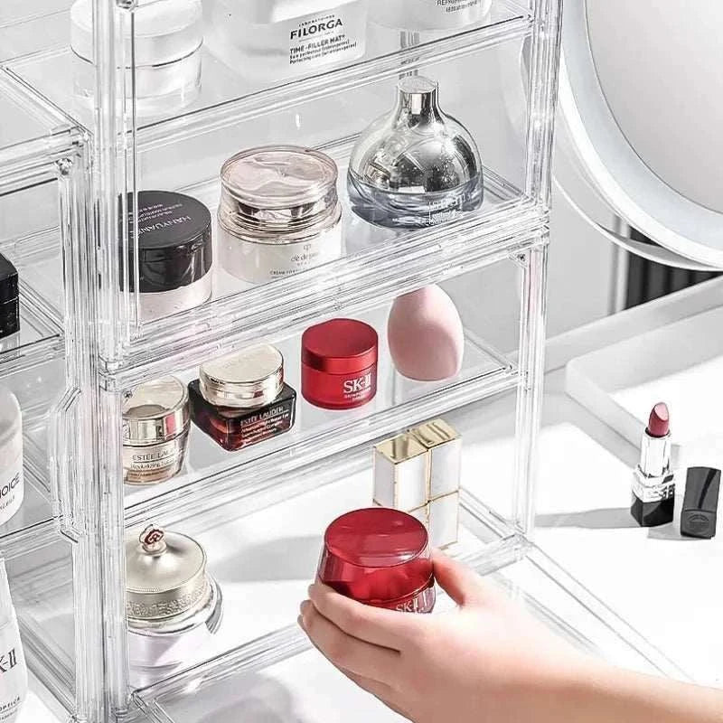 Transparent Acrylic Organizer with clear compartments holding various skincare and cosmetic containers on a white surface, with a hand reaching for a red jar